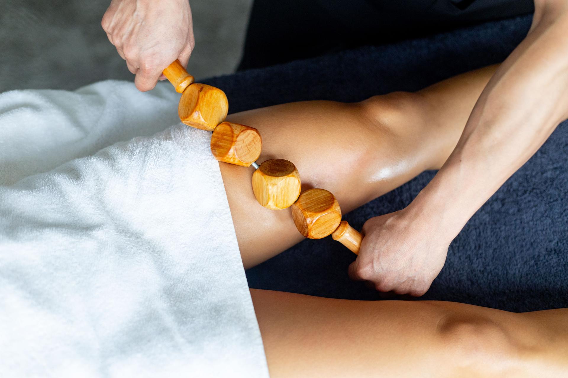 Masseur using wooden tool massaging woman leg in spa