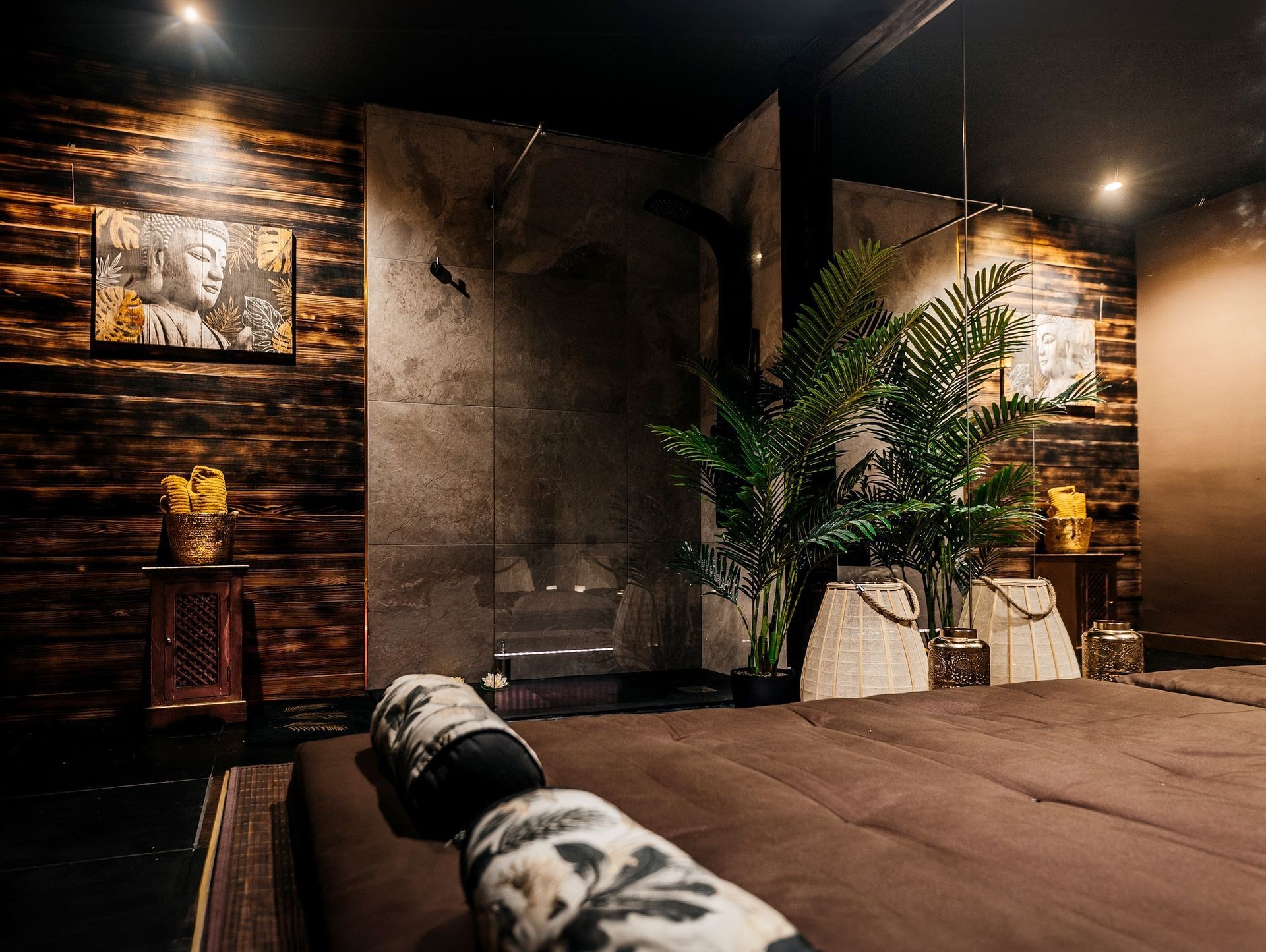Relaxing spa room with wooden walls, plants, and calming Buddha artwork, softly lit atmosphere.