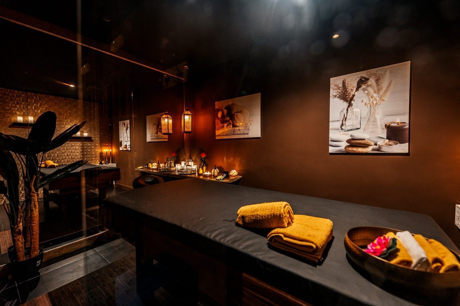 Cozy spa room with massage table, warm lighting, candles, and decorative art on walls.