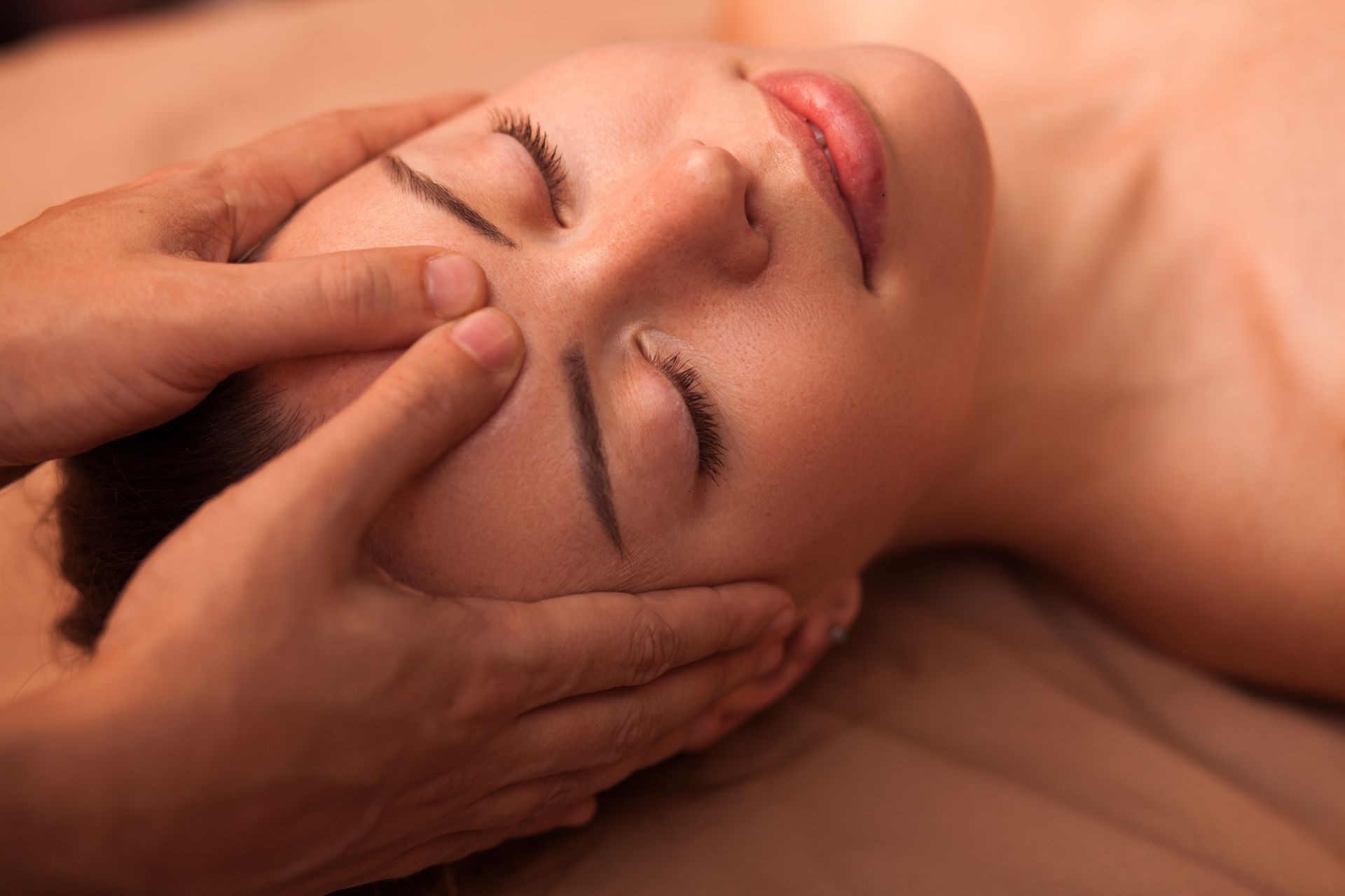 Close up of a happy beautiful woman smiling with her eyes closed, receiving soothing head massage. Young attractive woman enjoying Skull facial massage at Marbella Zen Spa.