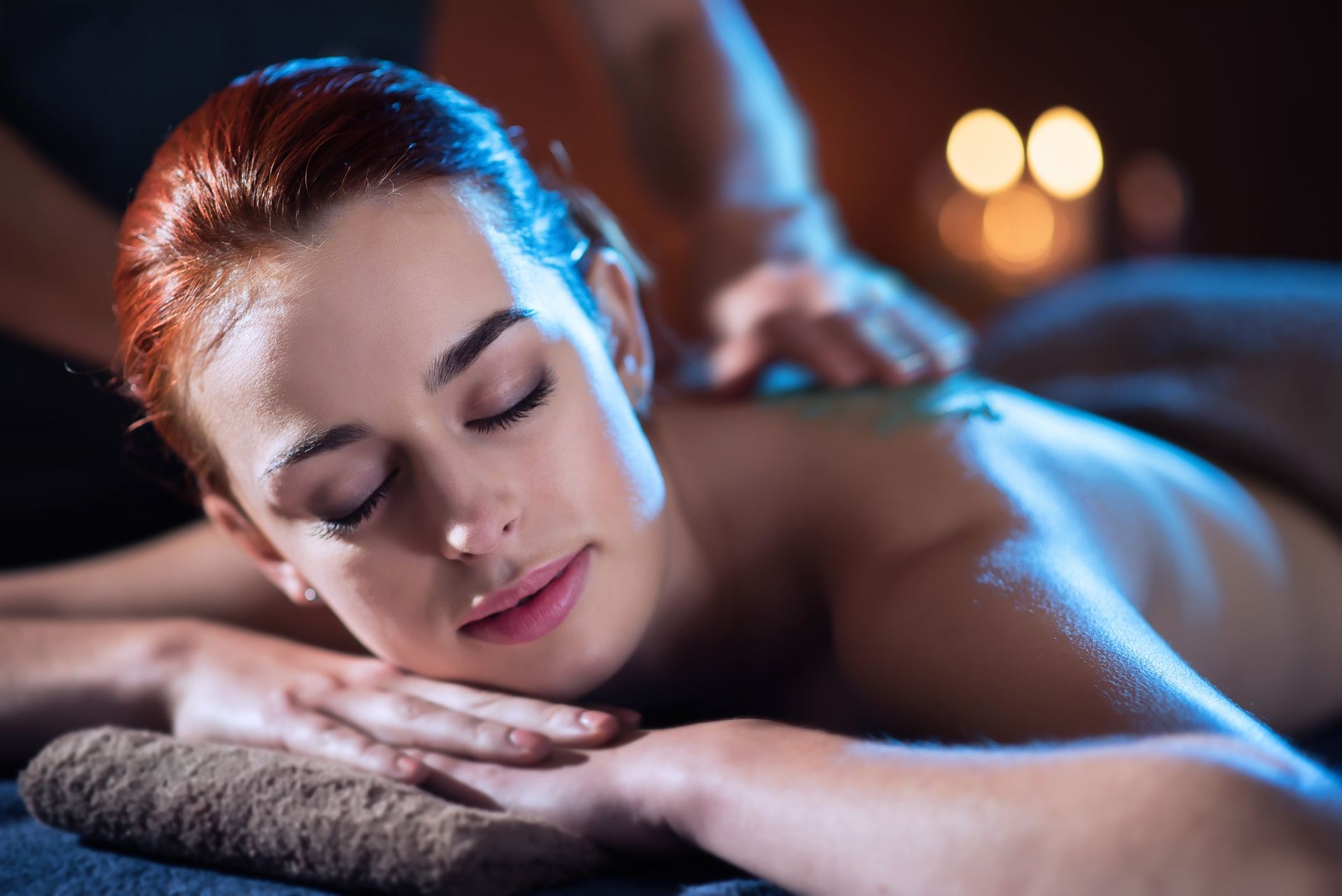 A beautiful young woman lying on a massage table in a beauty salon, while a therapist apply a scrub on her back