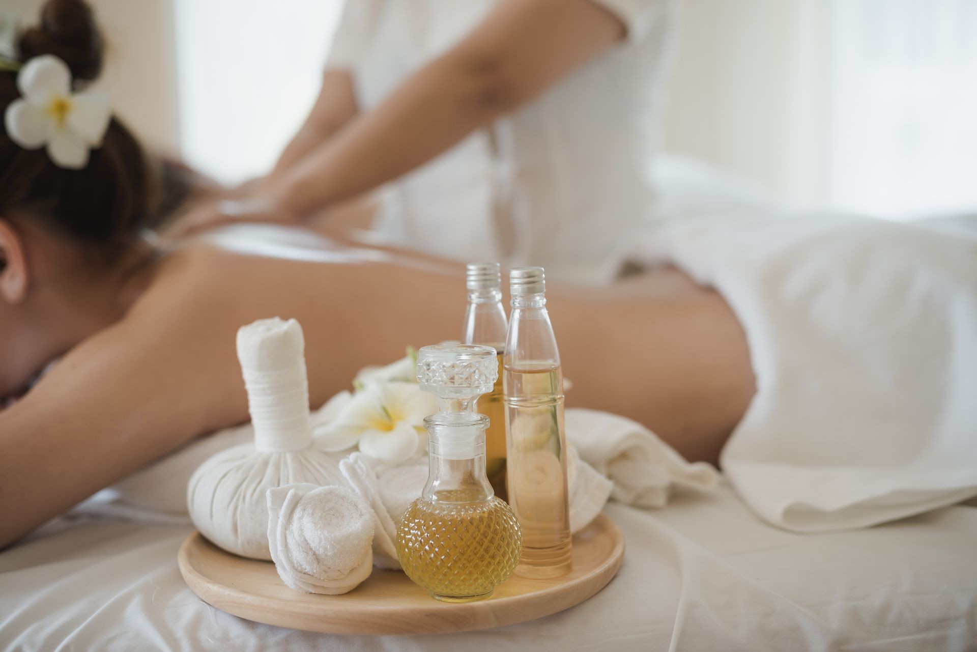 Botellas de aceites esenciales en una bandeja de madera. fondo Joven hermosa mujer jóven relajándose con un masajel balinés en Marbella Zen Spa